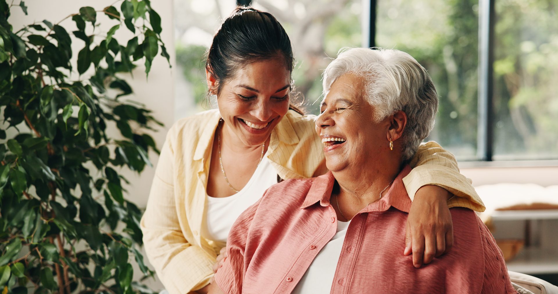 Caregiver and senior woman laughing together by a bright window at home